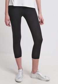 Leggings capri negros hechos de un material elástico y suave. Presentan un diseño ajustado que termina a mitad de pantorrilla y se combinan con zapatillas plateadas.