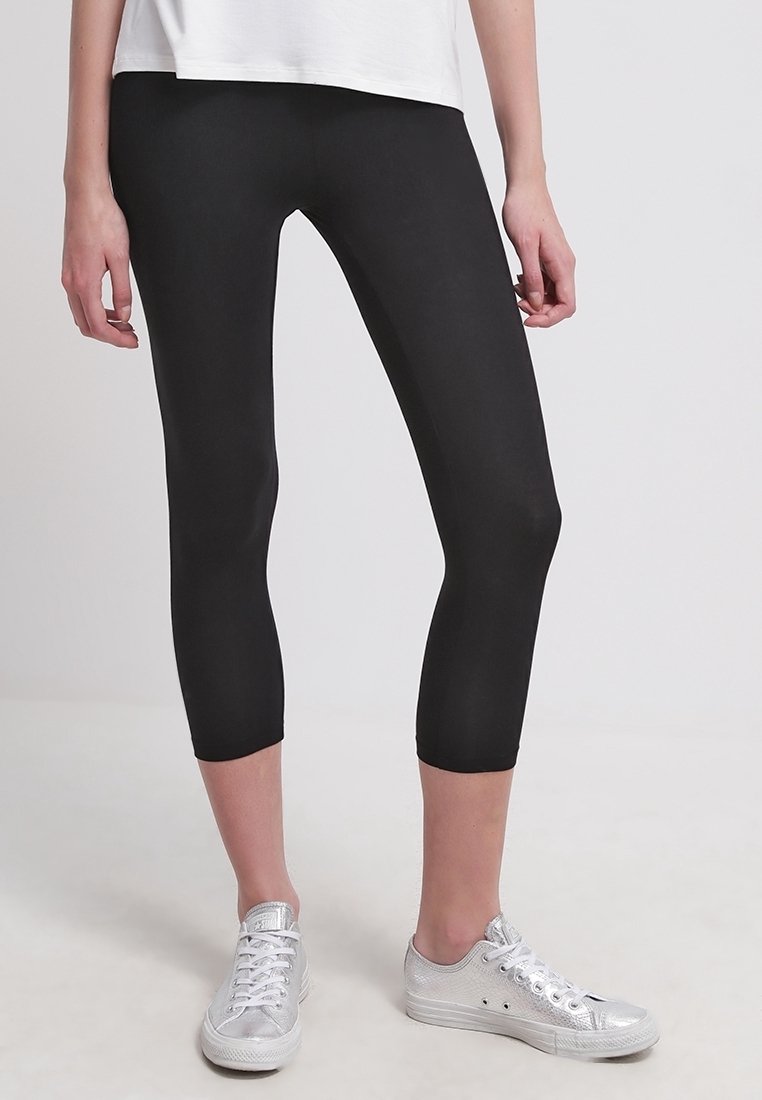 Leggings capri negros hechos de un material elástico y suave. Presentan un diseño ajustado que termina a mitad de pantorrilla y se combinan con zapatillas plateadas.