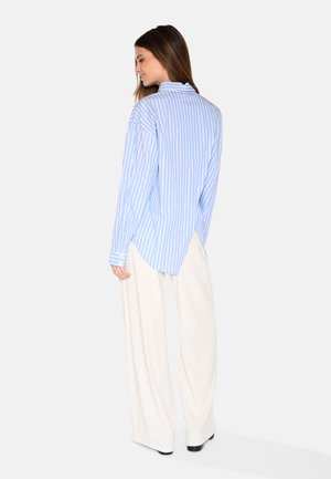 Camicia azzurro chiaro a maniche lunghe con strisce verticali bianche, vestibilità rilassata e orlo arrotondato, abbinata a pantaloni larghi color avorio.