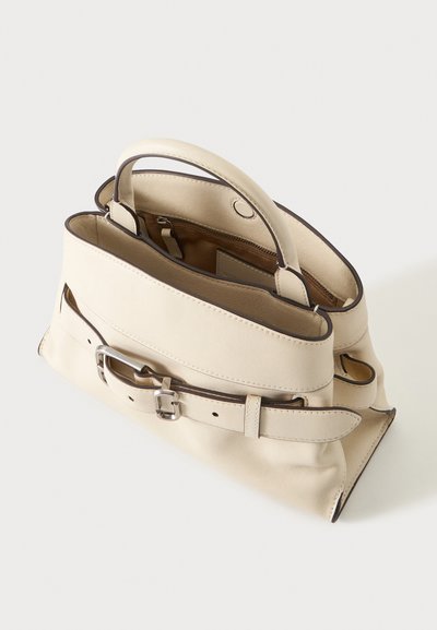 Sac à main en cuir crème avec des poignées supérieures, une sangle avant à boucle, et une fermeture éclair partiellement ouverte révélant la doublure intérieure et la poche.