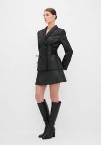 Blazer nero текстurizzato con design doppiopetto, vita strizzata, abbinato a una gonna mini coordinata e stivali neri con tacco al ginocchio.