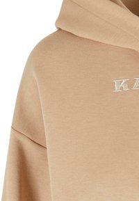 Felpa beige con texture a coste, dotata di un grande cappuccio e logo ricamato in bianco sporco. Vestibilità oversize con cuciture delle spalle cadenti.
