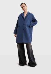 Modrý vlnený kabát s klopovým golierom, zapínaním na gombík a dvoma prednými vreckami. Má voľný strih a dlhé rukávy.