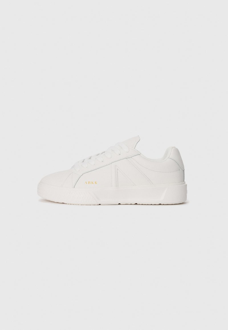 Sneaker bianca a bassa altezza con design stringato, suola texturizzata e sottile branding dorato "ARKK" sul lato.