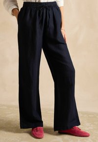 Tumesinised laia säärega püksid elastse vöökoha ja nööriga, valmistatud pehmest kangast. Sobitatud roosade slip-on-kingadega mustrilisel põrandal.