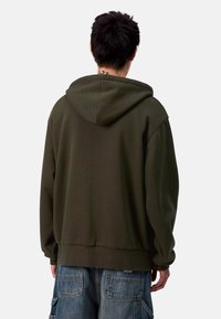 Felpa verde oliva con cappuccio ampia, polsini e orlo a coste, e una texture morbida. La vista posteriore mostra cuciture minime e un design semplice.