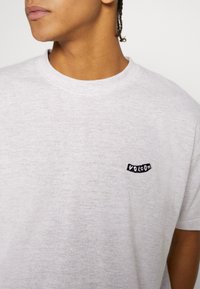 Svetlošedé tričko vyrobené z mäkkej látky, s čiernou vyšitou logom "Volcom" na ľavej strane hrudníka. Klasický dizajn s okrúhlym výstrihom.