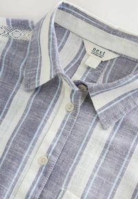 Camicia di lino con righe verticali blu e bianche, colletto e chiusura con bottoni, con un sottile dettaglio in pizzo sulla spalla.