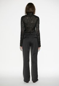 Schwarzes Spitzenoberteil mit langen Ärmeln und floralem Muster, kombiniert mit schwarzen hoch taillierten, weit geschnittenen Hosen, die eine glatte Textur und eine figurbetonte Silhouette präsentieren.