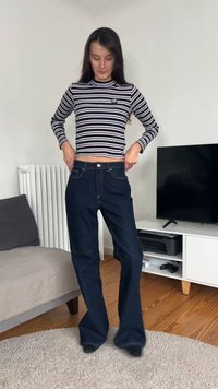 Jeans azul-escuro com corte flare combinados com um top de mangas compridas às riscas pretas e brancas com um pequeno logótipo. O denim apresenta costuras visíveis e bolsos.