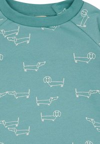 Türkises Baumwoll-T-Shirt mit einem sich wiederholenden Muster von weißen Dackeln. Das Design umfasst einfache Umrisse und ausdrucksstarke Gesichter.