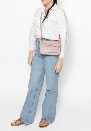 Borsa a tracolla in pelle rosa chiaro con superficie testurizzata, hardware dorato e tasca frontale. Indossata con jeans blu casual e sandali.