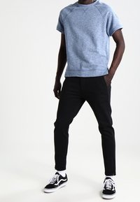 Sweat-shirt bleu chiné à manches courtes, associé à un pantalon noir slim et des baskets noir et blanc avec des lacets blancs.