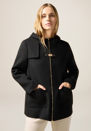 Abrigo negro con capucha y cierre frontal de cremallera, con dos bolsillos laterales, detalles en dorado y tejido texturizado. Líneas limpias y diseño minimalista.