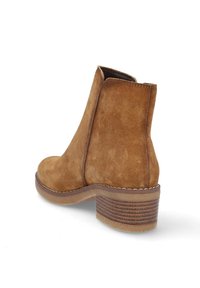 Bota de tobillo de ante marrón con puntera redondeada, tacón bloque de altura media y costuras claras contrastantes a lo largo de la suela. Textura suave.
