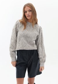 Maglione grigio con texture e motivo a foglia, scollatura rotonda e maniche a sbuffo, abbinato a pantaloni shorts in pelle nera, con dettagli delle tasche a vista.