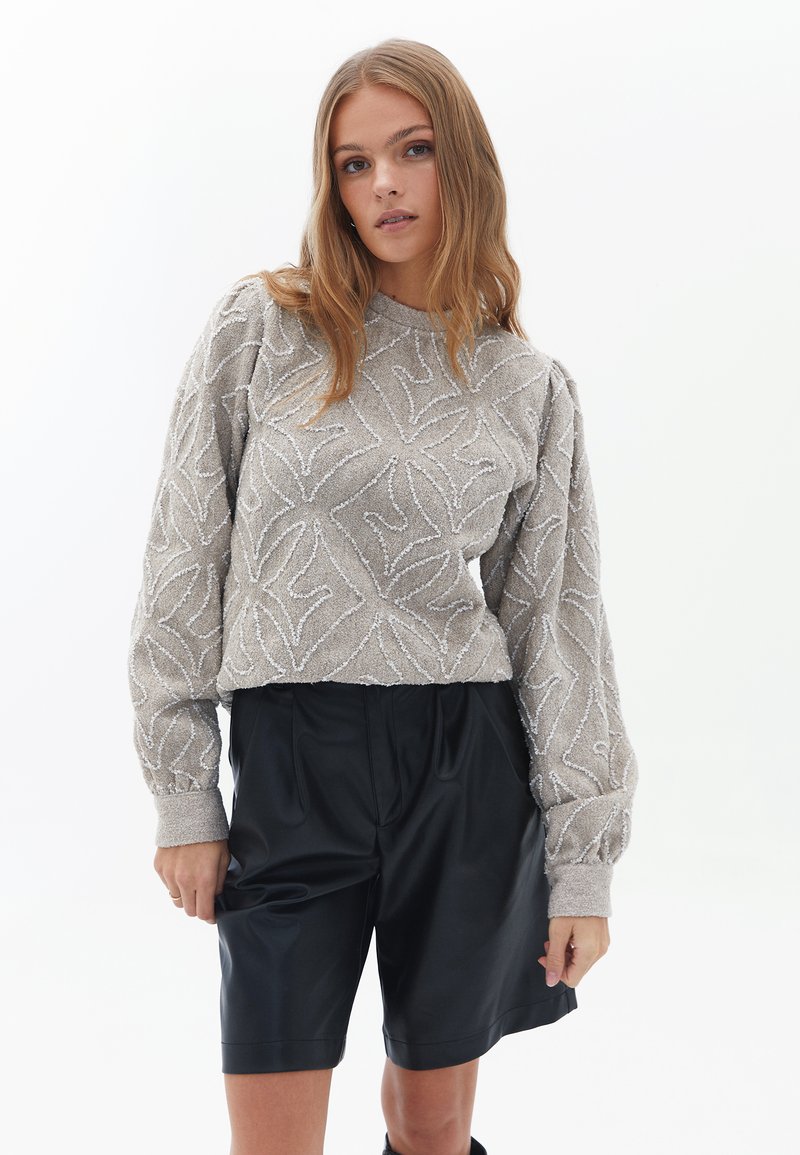 Maglione grigio con texture e motivo a foglia, scollatura rotonda e maniche a sbuffo, abbinato a pantaloni shorts in pelle nera, con dettagli delle tasche a vista.