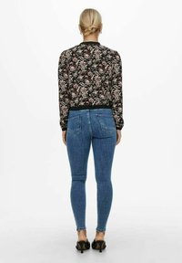 Blomsterprydd svart bomberjacka med en ribbad krage, kombinerad med åtsittande blå denimjeans och svarta stilettklackar.