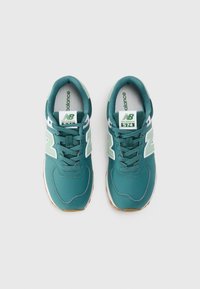 Teal värvi New Balance 574 spordijalatsid, milles on valged ja helesinised aktsendid, nähtud ülalt lihtsalt taustal.