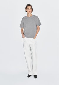 Grå kortærmet t-shirt med afslappet pasform, parret med hvide brede bukser og sorte spidse sko; minimalistisk design.