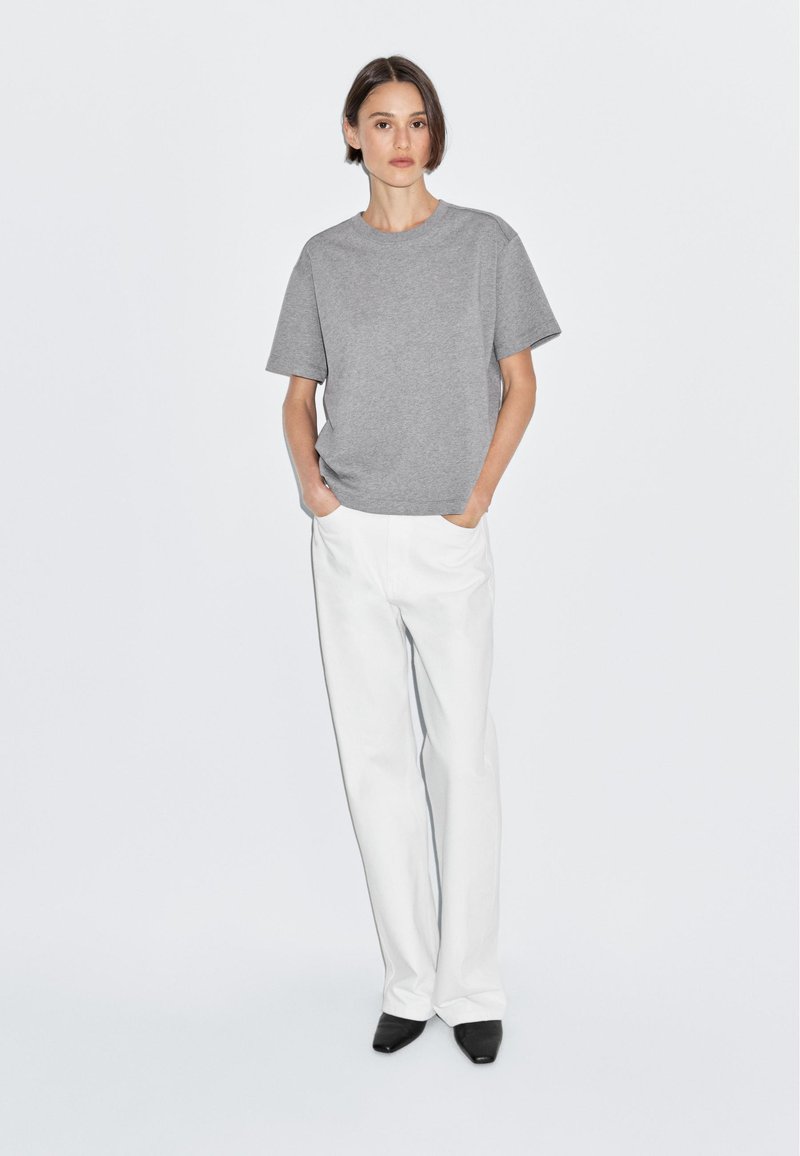 Grå kortærmet t-shirt med afslappet pasform, parret med hvide brede bukser og sorte spidse sko; minimalistisk design.