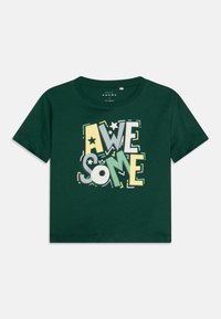 Grønn bomulls t-skjorte med et stort, fargerikt trykt design med ordet "AWESOME" i varierende fonter og størrelser, inkludert stjerner og detaljer.