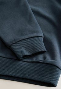 Sudadera de color azul oscuro con tejido que presenta un puño acanalado y textura suave, con ligeras arrugas que aportan un aspecto relajado.