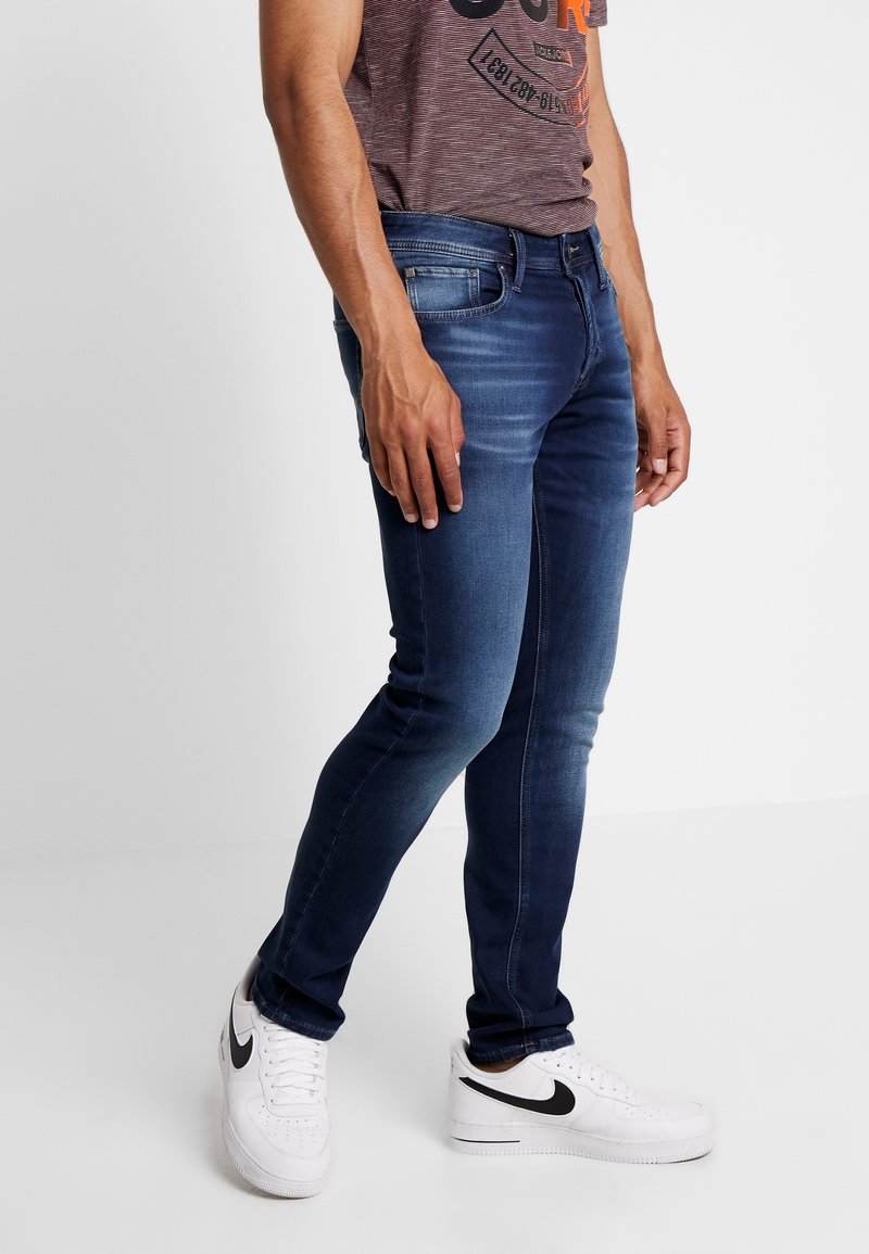 Mörkblå slim-fit jeans i denim, med en blekningseffekt, fem fickor och vita sneakers med en svart logotyp.