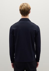 Maglia a maniche lunghe in blu navy scuro con tessuto liscio e leggero, dotata di colletto e polsini con bottoni. Design semplice e lineare.