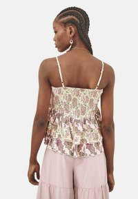 Top sin mangas de peplum floral con espalda fruncida, que presenta patrones en crema, verde y púrpura. Acentuado con tirantes delgados y capas con volantes.