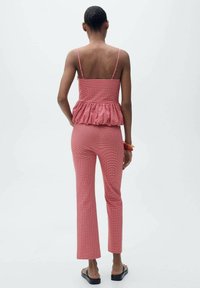Zweiteiliges Outfit im rot karierter Muster; tailliertes Oberteil mit Peplum-Detail und schmal geschnittene Hose, kombiniert mit flachen schwarzen Sandalen.