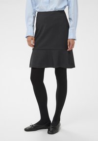 Jupe grise évasée en tissu au toucher lisse, associée à des collants noirs et des chaussures plates noires, dotée d'un léger volant au bas.