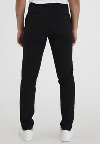 Schwarze Hose mit schmaler Passform, ausgestattet mit zwei Gesäßtaschen und Gürtelschlaufen. Kombiniert mit weißen Sneakers für einen lässigen Look.