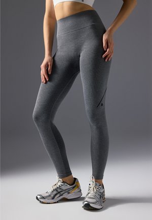 Gray high-waisted leggings with textured patterns and sleek design, featuring a side pocket and ribbed detailing. Paired with athletic shoes.