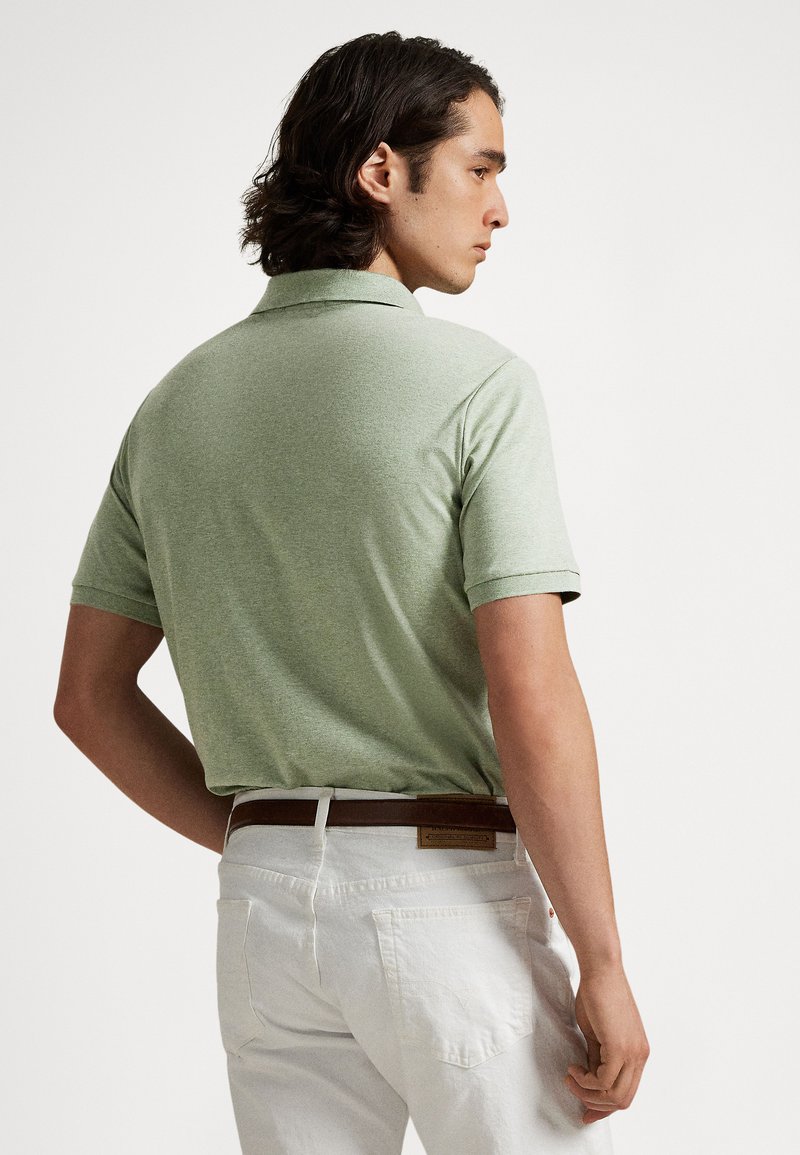 Grünes kurzärmeliges Polohemd mit strukturierter Oberfläche, kombiniert mit weißen Hosen und einem braunen Ledergürtel. Ansicht von hinten, die Details des Kragens zeigt.