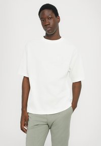White short-sleeve t-shirt with crew neckline, featuring a subtle embossed "MK" logo on the chest. Material appears smooth and lightweight.