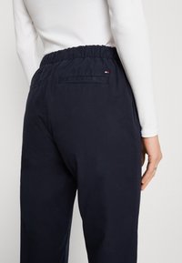 Námořnicky modré bavlněné kalhoty s elastickým pasem, s kapsou vzadu a decentním logem. Hladká textura, volný střih.