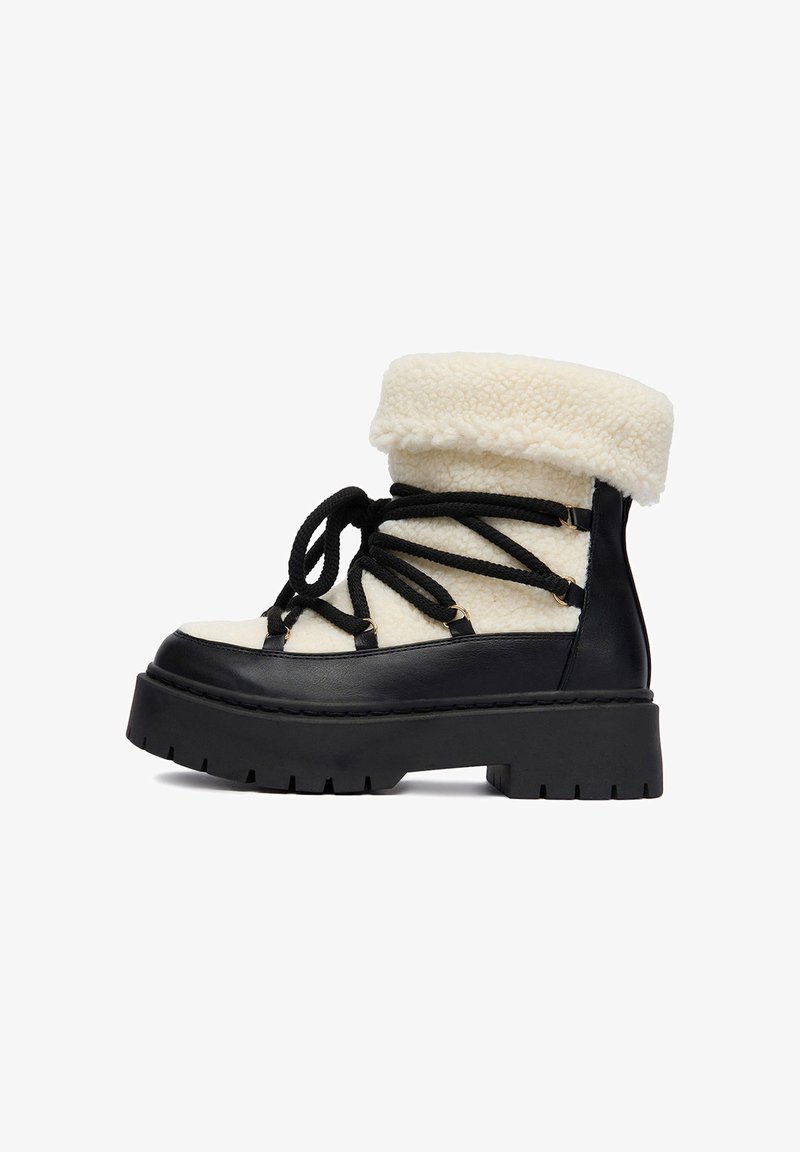 Kremowe botki za kostkę wyłożone sherpa, z czarną grubą podeszwą i czarnymi krzyżującymi się sznurówkami, zaprojektowane z myślą o zimie.