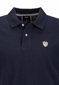 Marineblauw polo shirt van een gestructureerde stof, met twee knopen en een klein geborduurd schildlogo. Heeft een gestreepte kraag binnenvoering.