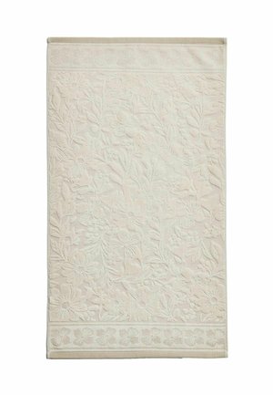 Serviette de bain couleur crème avec un motif floral et feuillu en relief couvrant la majeure partie de sa surface et de ses bords.