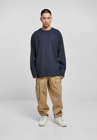 Marineblå langermet t-skjorte med avslappet passform, sammen med beige cargo-bukser med sidelommer, fullført med hvite sneakers.