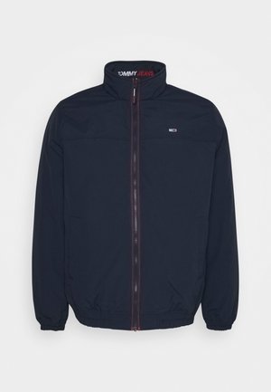 Marineblauwe, ritsjack met een hoge kraag, elastische manchetten en zoom. Voorzien van een logo op de borst en "TOMMY JEANS" gedrukt aan de binnenkant van de kraag.