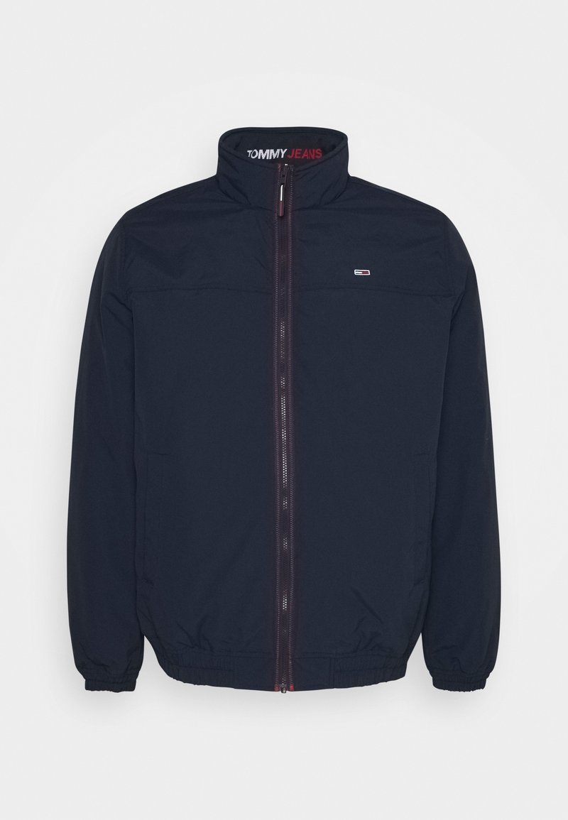Granatowa kurtka zapinana na zamek z wysokim kołnierzem, elastycznymi mankietami i dołem. Posiada logo na piersi oraz napis "TOMMY JEANS" wydrukowany wewnątrz kołnierza.