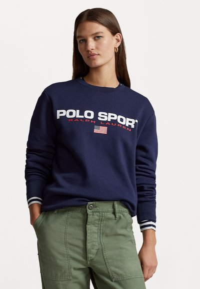 Sweater bleumarin cu "POLO SPORT" și un logo cu steagul american în alb și roșu. Are manșete cu dungi și un gât clasic de tip crew.