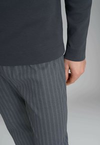 Maglietta grigia scura a maniche lunghe con una texture liscia, abbinata a pantaloni grigi con un motivo a zigzag in grigio chiaro.