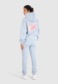 Sudadera azul clara con un gran gráfico rosa en la parte trasera, combinada con pantalones de chándal a juego; tejido suave y diseño de corte relajado.