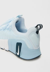 Šviesiai mėlynos sportinės bateliai su tekstūruotu viršutiniu sluoksniu, storu baltu padu ir tamsiai mėlynu akcentu su baltu Nike logotipu šone.