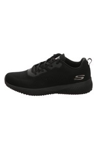 Scarpa sportiva nera con texture a coste, design con lacci e linguetta. Presenta un prominente logo 'S' sul lato. Suola in gomma.