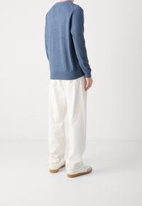 Maglione blu lavorato a maglia, maniche lunghe, polsini e orlo a coste, abbinato a pantaloni bianchi in cotone larghi. Sneakers con suola in gomma, dettagli bianchi e grigi.