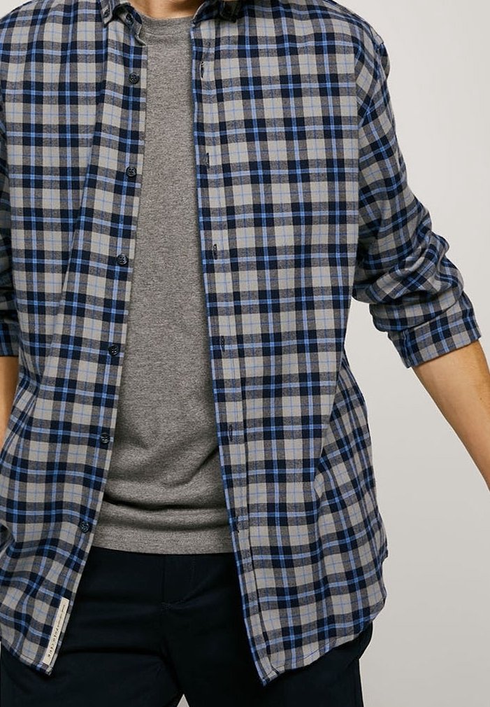 Camicia a maniche lunghe con motivo a quadri blu e grigio, con le maniche arrotolate, indossata sopra una t-shirt grigia, caratterizzata da una vestibilità comoda e un tessuto morbido.